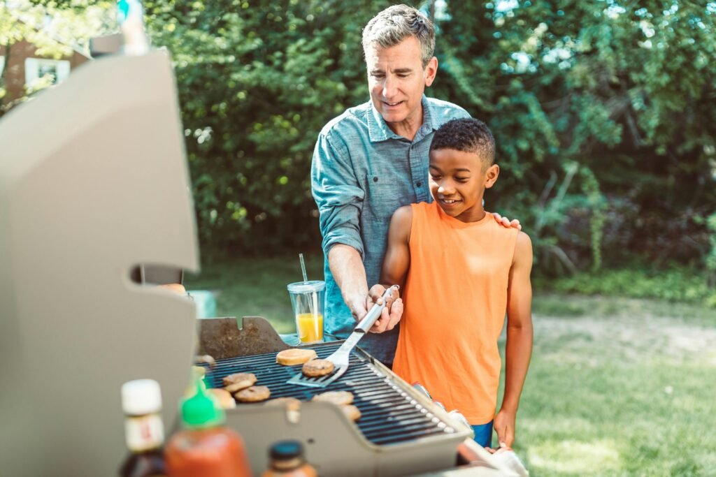 Father teaching son to grill burgers on a sunny day outdoors, fostering family bond.